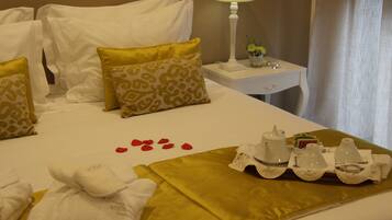 Un letto d'hotel rifatto con lenzuola bianche e dorate, un comodino con una lampada e un vaso di fiori, e un vassoio con articoli da toilette.