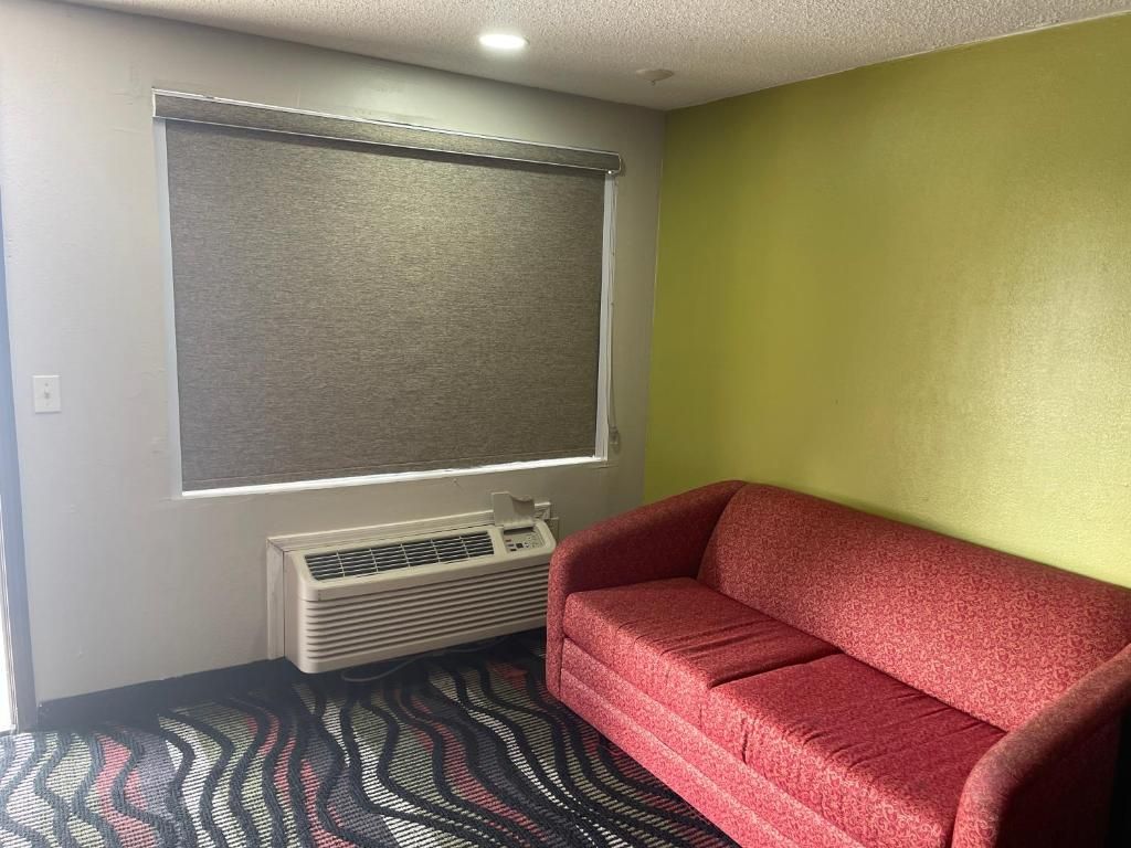 A room with a red sofa, a window with a blind, a radiator, and a patterned carpet.
