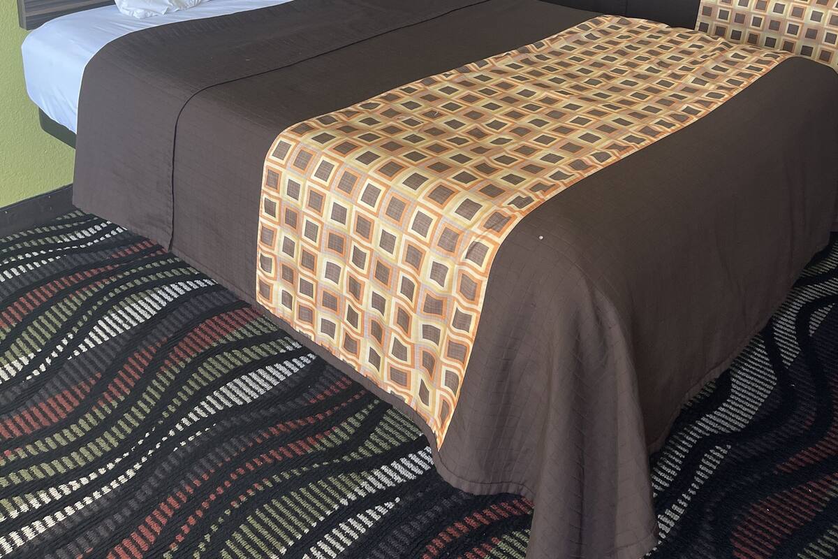 A hotel room with two beds, a headboard with a light fixture, and a patterned carpet.