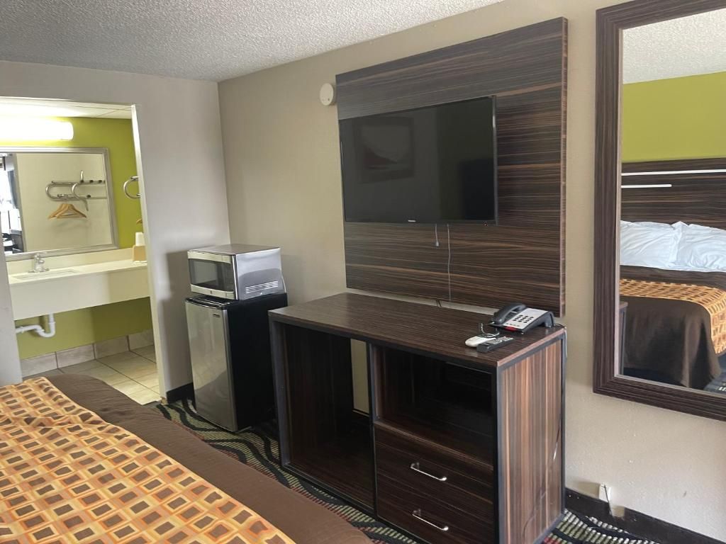 A hotel room with a bed, a desk with a flat-screen TV, a minibar, and a mirror.