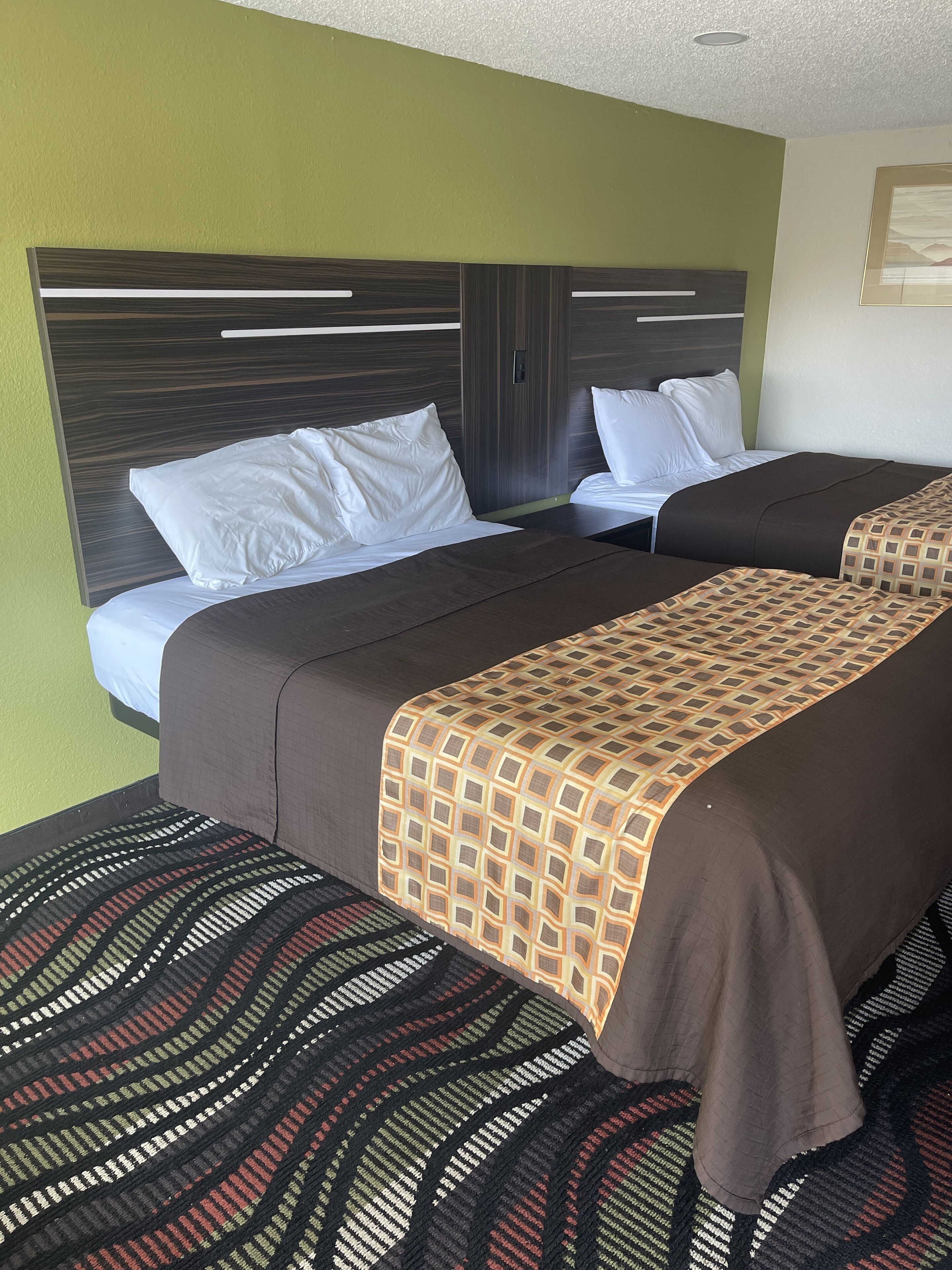 A hotel room with two beds, a headboard, and a patterned rug.