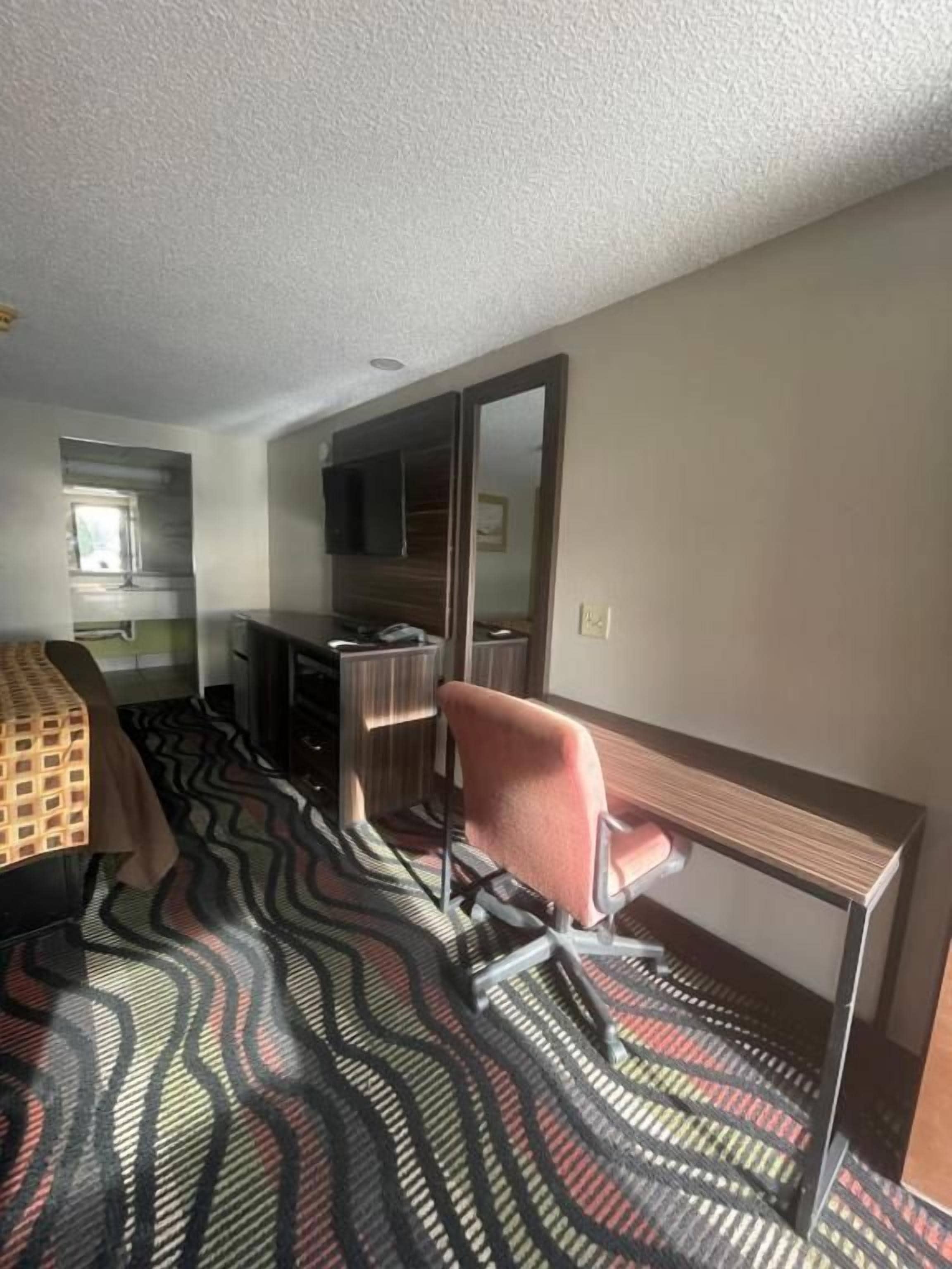 A hotel room with a bed, a desk, a chair, a mirror, and a patterned carpet.