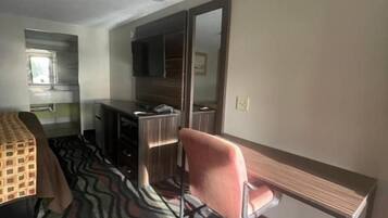 A hotel room with a bed, a desk, a chair, a mirror, and a patterned carpet.