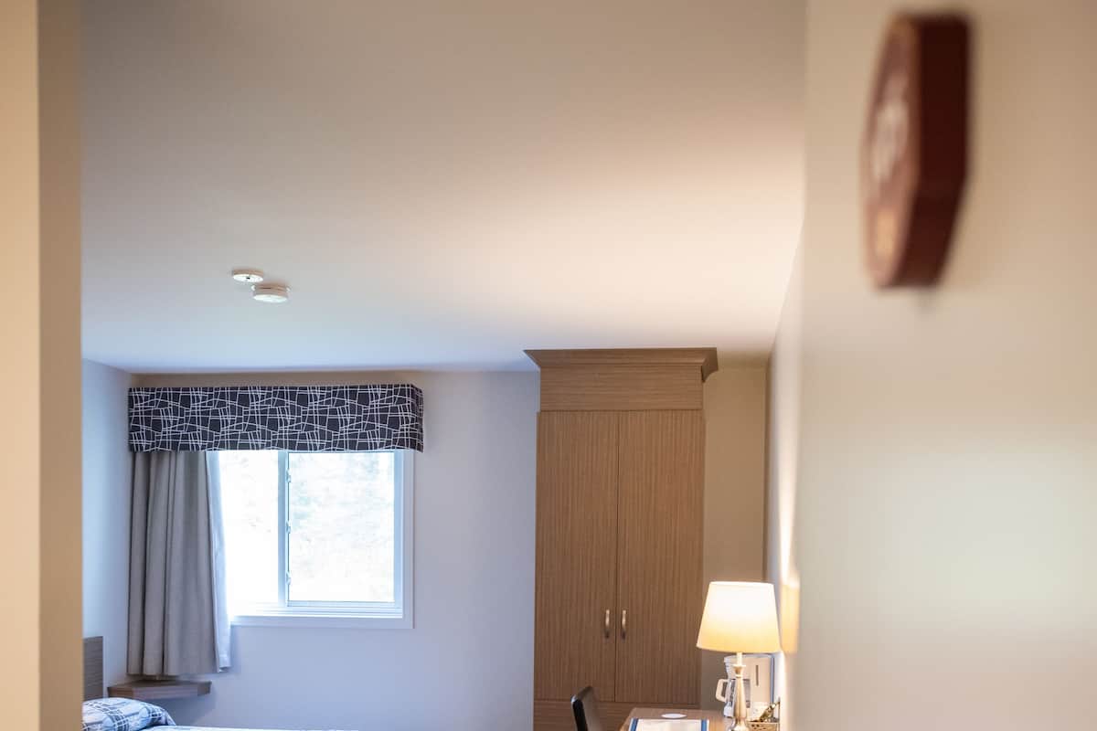 A hotel room with two beds, a desk with a lamp, a chair, and a wardrobe.
