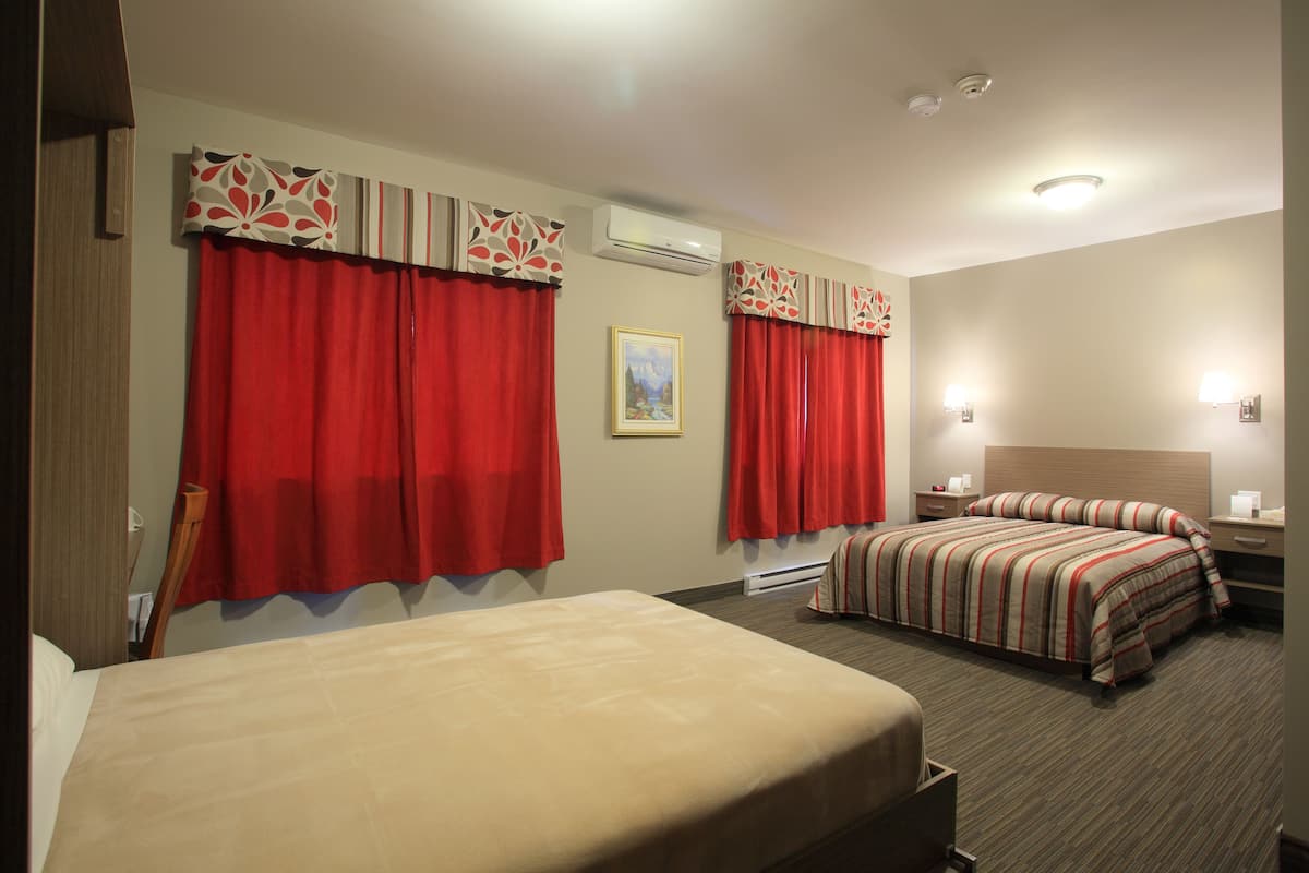 A hotel room with two beds, red curtains, a painting, and a bedside table with a lamp.
