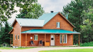 A wooden cabin with a green roof, a porch with two chairs, and a number '190' on the door. - Ermitage Saint-Antoine (Lac-Bouchette)