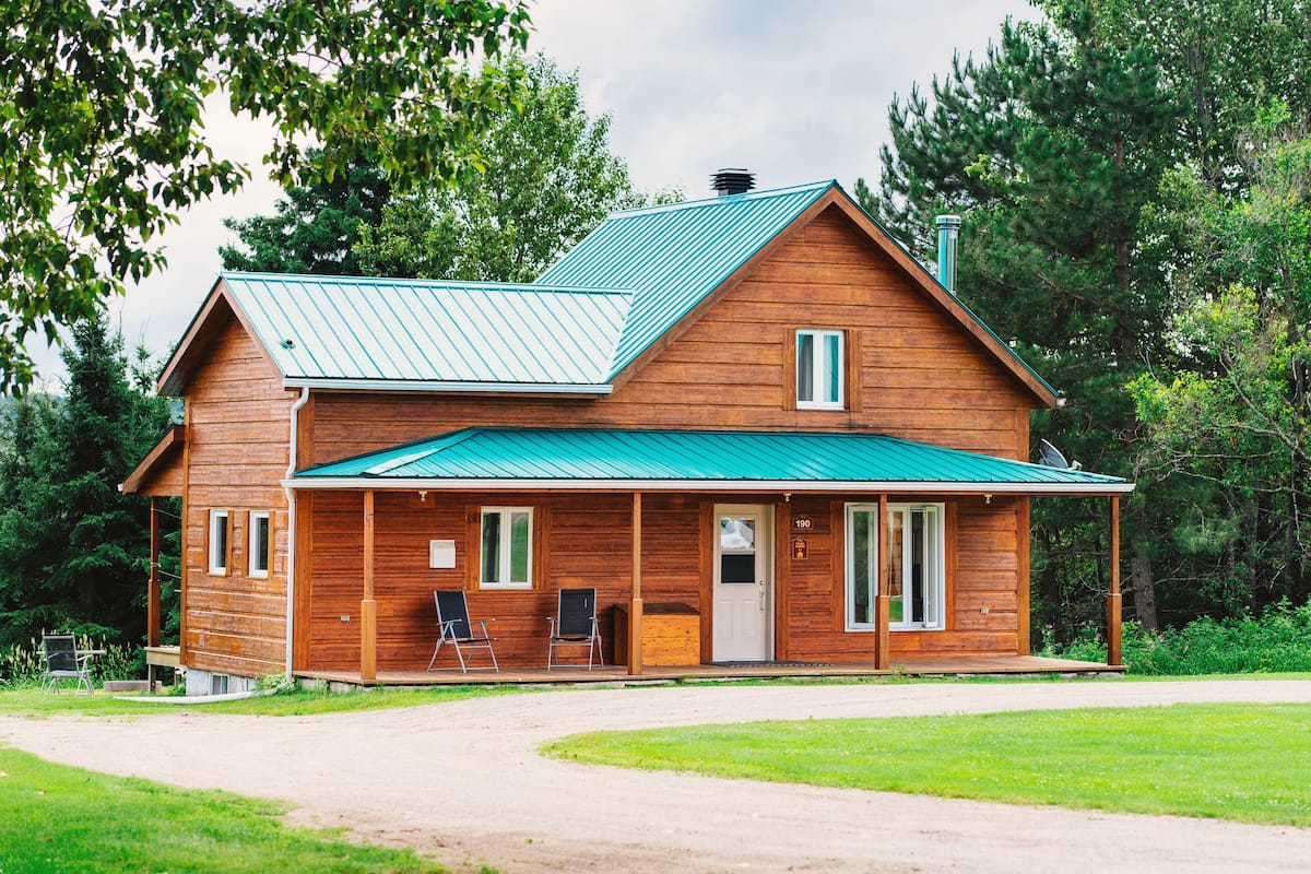 A wooden cabin with a green roof, a porch with two chairs, and a number '190' on the door.