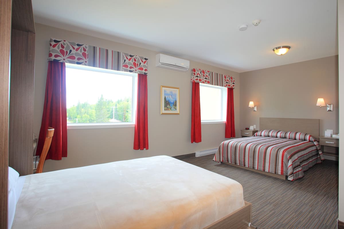 A hotel room with two beds, red curtains, a painting, and a window with a view of trees.