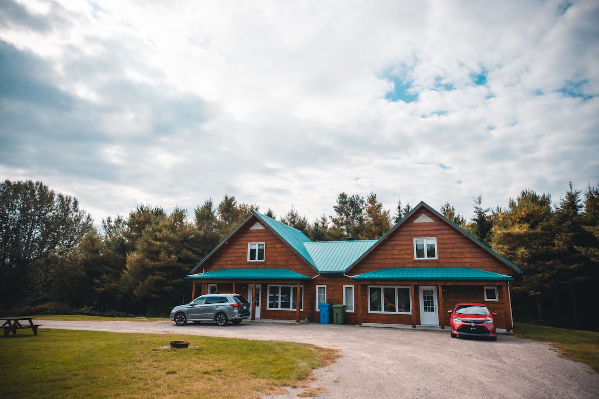 A cabin with a green roof, two cars parked in front, and a picnic table nearby.