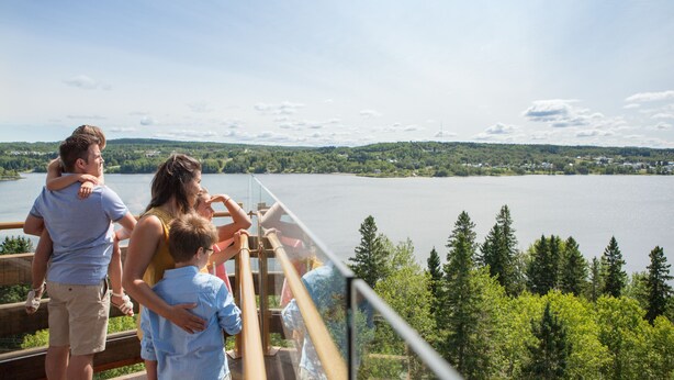 A family on a scenic overlook with a lake and forested hills in the background. - Ermitage Saint-Antoine (Lac-Bouchette)