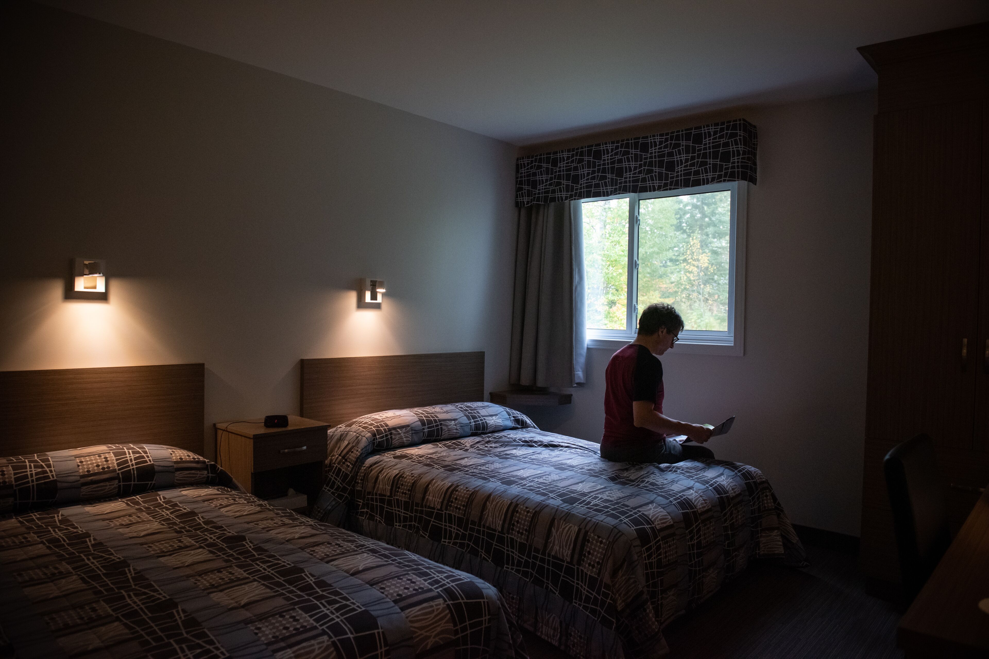 Habitación de hotel con dos camas, una mesita de noche, un escritorio y una ventana con cortinas.