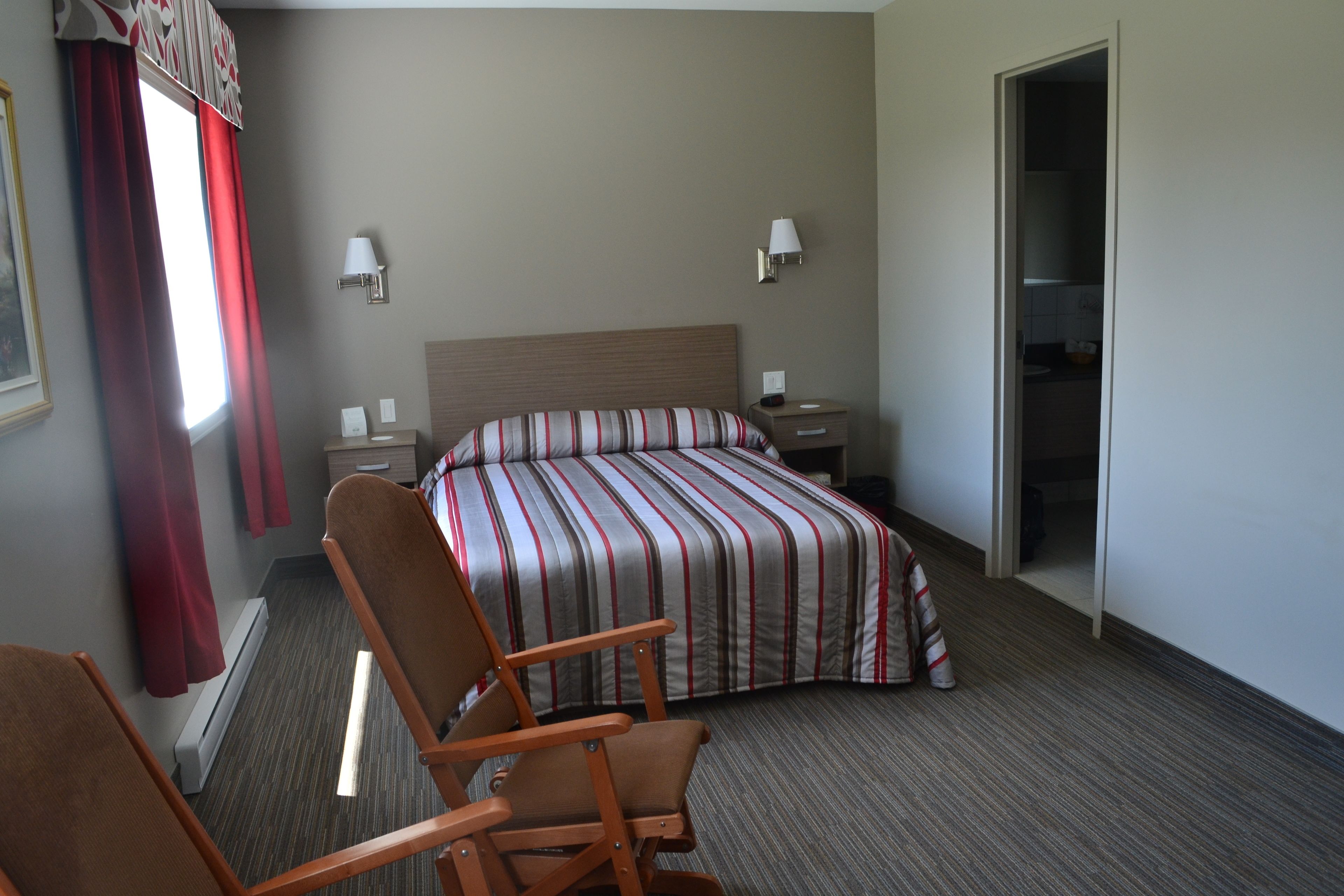 A hotel room with a bed, a chair, a nightstand, and a door leading to a bathroom.