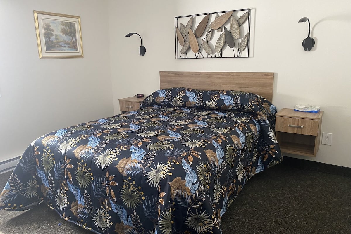A neatly made bed with a floral-patterned bedspread, a wooden headboard, bedside tables with lamps, and a framed picture on the wall.