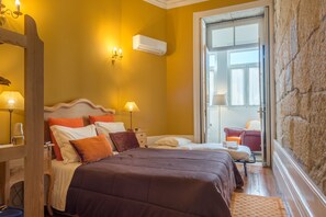 A hotel room with a large bed, two bedside tables with lamps, a wooden headboard, and a stone wall. - Centenary Fontainhas Apartments (Porto)