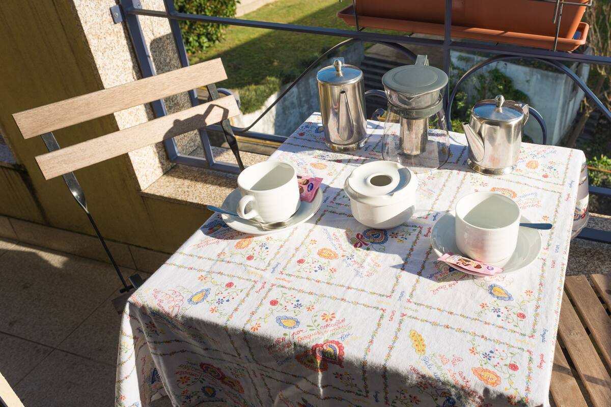 A balcony with a table set for tea, featuring a floral tablecloth and various tea utensils.
