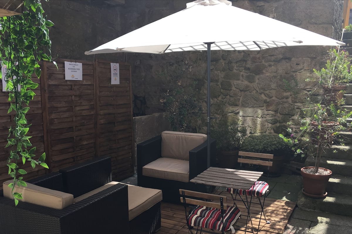 A patio area with wicker furniture, a white umbrella, and potted plants.