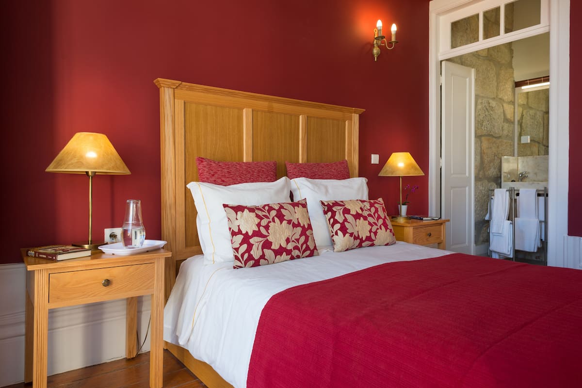 A neatly made bed with a red and white bedspread, two bedside lamps, and a wooden nightstand with a book and a glass.