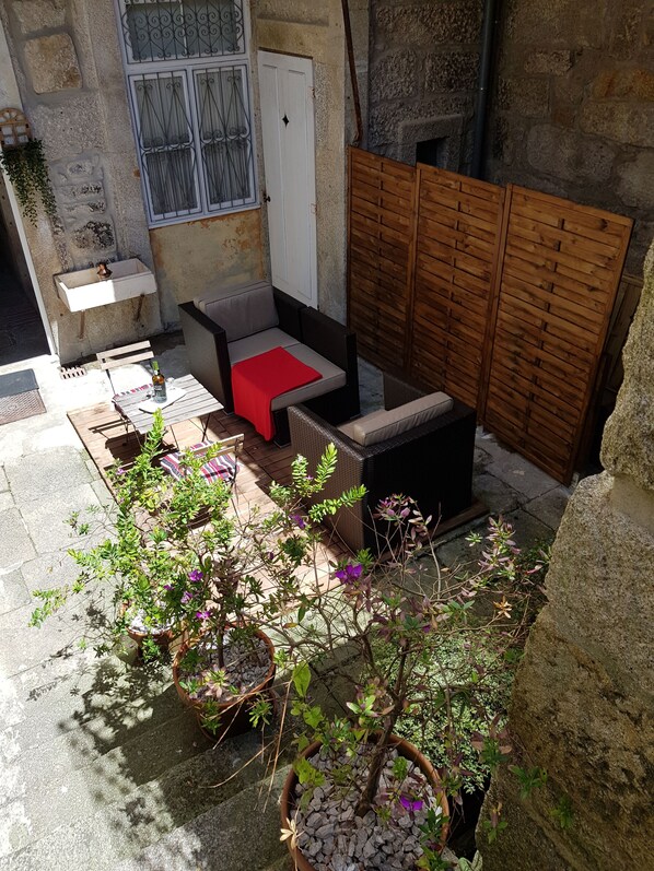 A small outdoor patio area with a wooden bench, a small table, and potted plants.