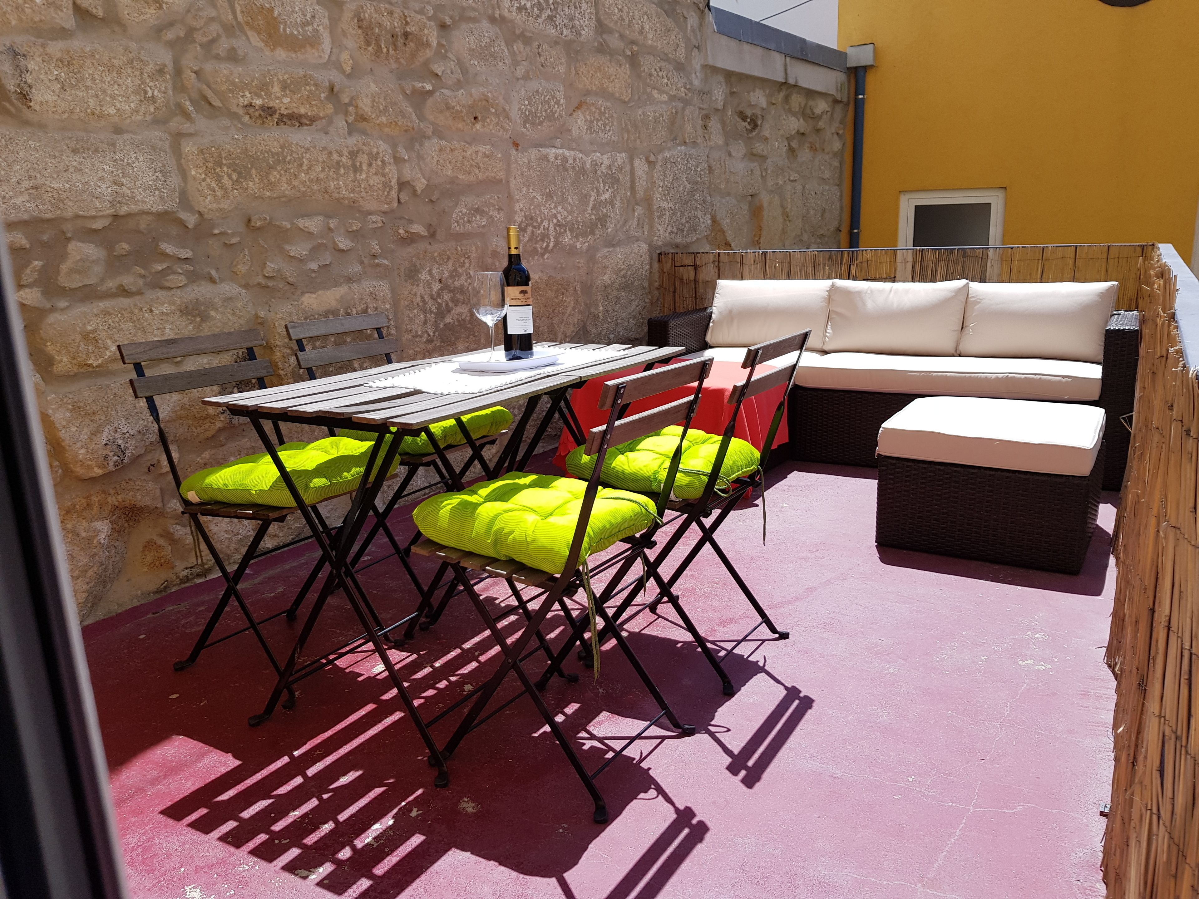 An outdoor patio with a stone wall, a table with chairs, and a sofa.