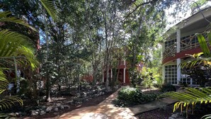 Uma trilha no jardim leva a um edifício com fachada vermelha e colunas brancas.