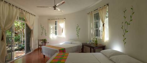 Habitación de hotel con dos camas, ventilador de techo y vistas al exterior.