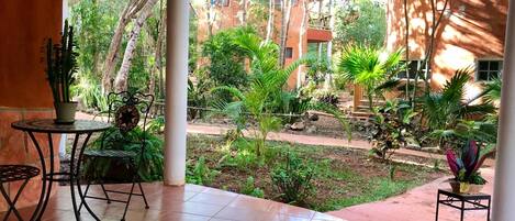A covered patio with tiled flooring, two metal tables with chairs, and potted plants.