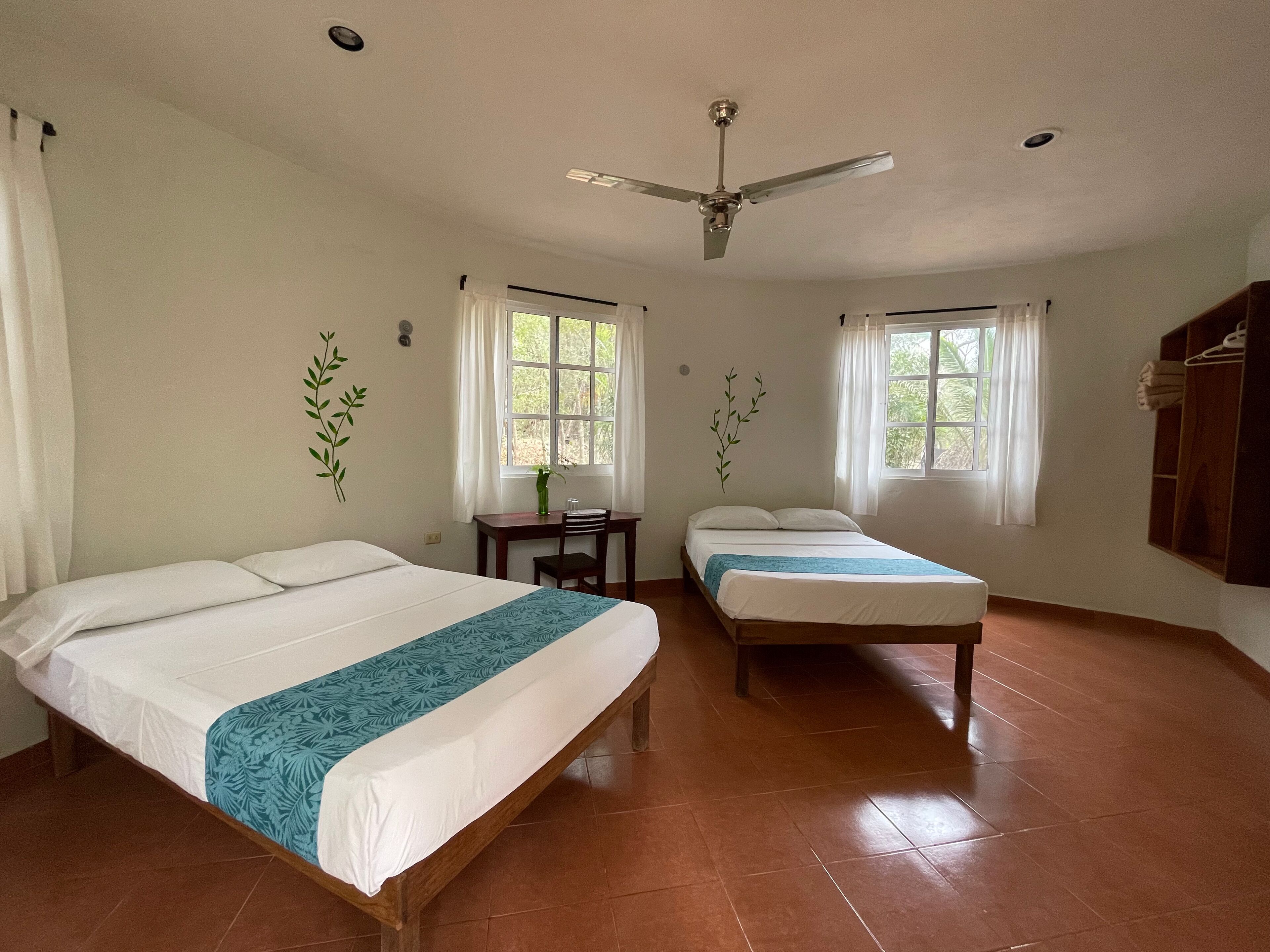 A room with two beds, a desk, a chair, and a ceiling fan.