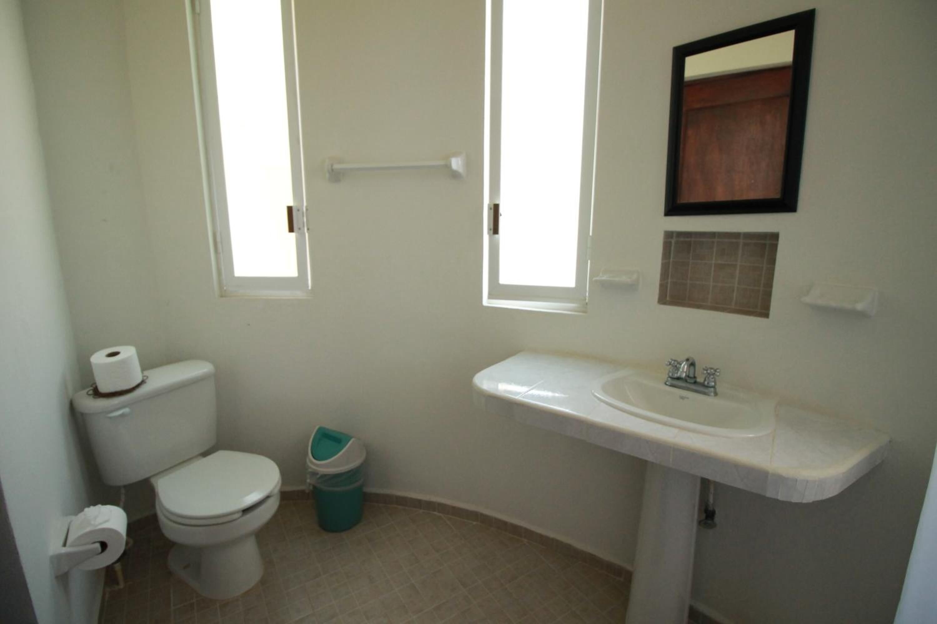 A small, clean bathroom with a toilet, sink, and two windows.