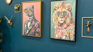 A room with a blue wall, two framed animal portraits, a mirror, and a small decorative item.