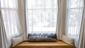 A window seat with a cushion featuring a cityscape design, curtains, and a view of buildings and a street. - 1906 Mission (San Francisco)