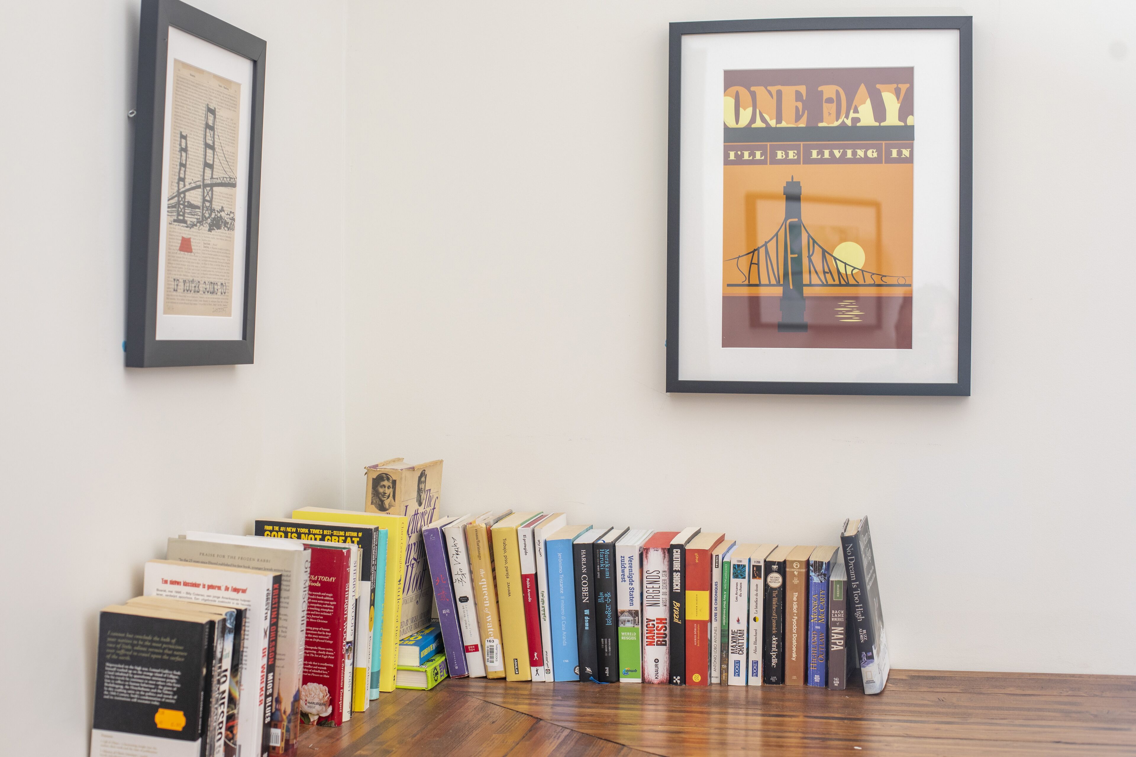 Um quarto com piso de madeira, um quadro com a imagem de uma ponte e uma fileira de livros na parede.