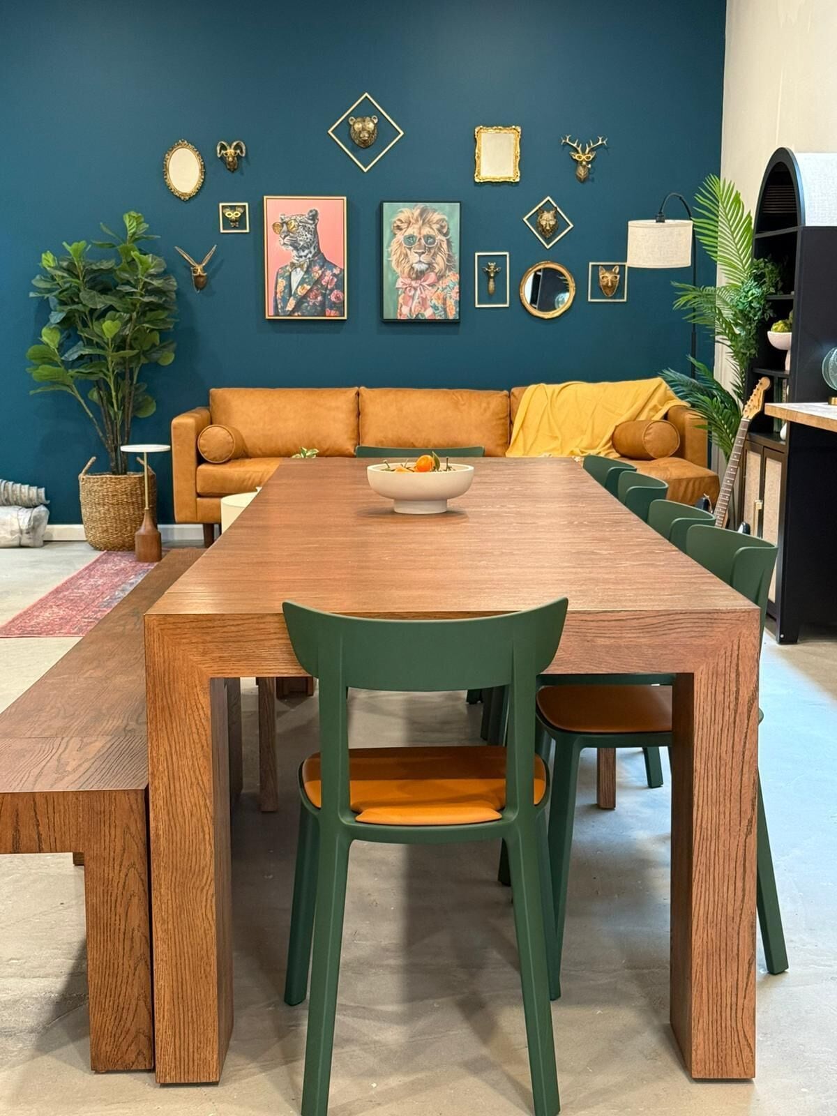 A dining area with a wooden table and green chairs, a sofa with yellow cushions, and wall-mounted decorations.