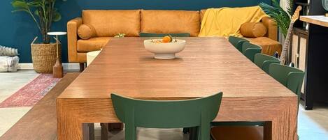 A dining area with a wooden table and green chairs, a sofa with yellow cushions, and wall-mounted decorations.