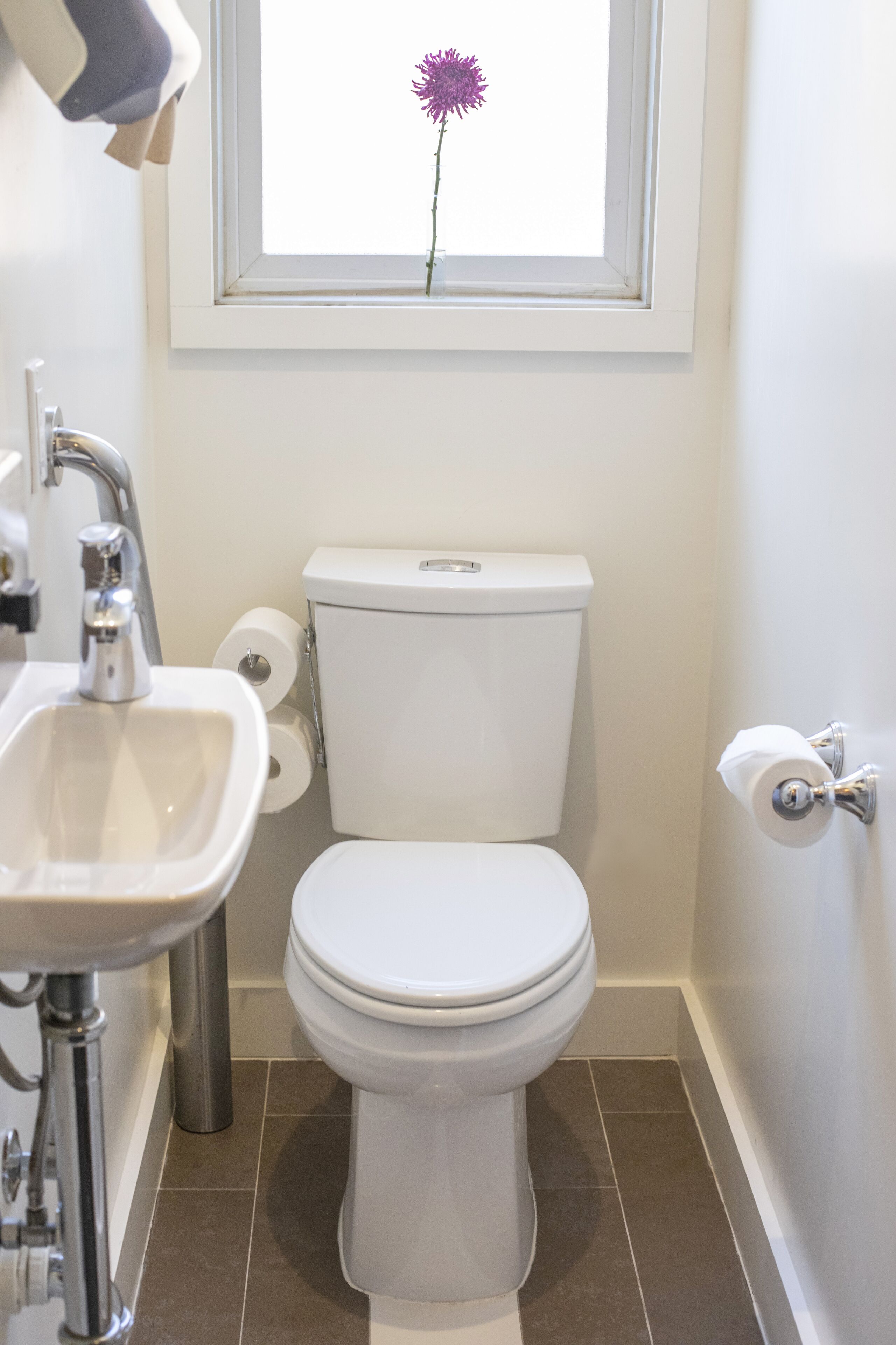 A bathroom with a toilet, sink, and a window with a flower.