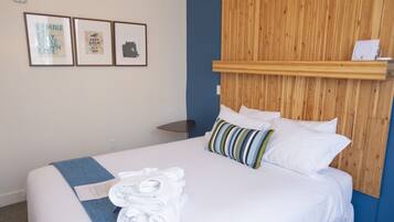 A neatly made bed with white linens and a blue towel, a wooden headboard, and three framed pictures on the wall.