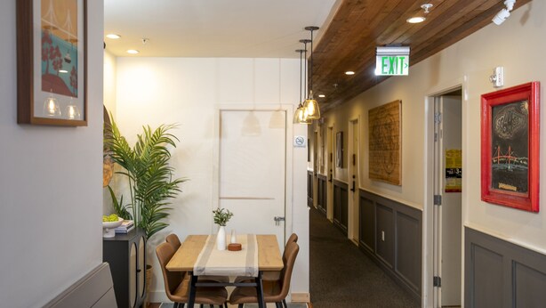 A hallway with a wooden ceiling, a table with chairs, a potted plant, and framed pictures on the walls. - 1906 Mission (San Francisco)