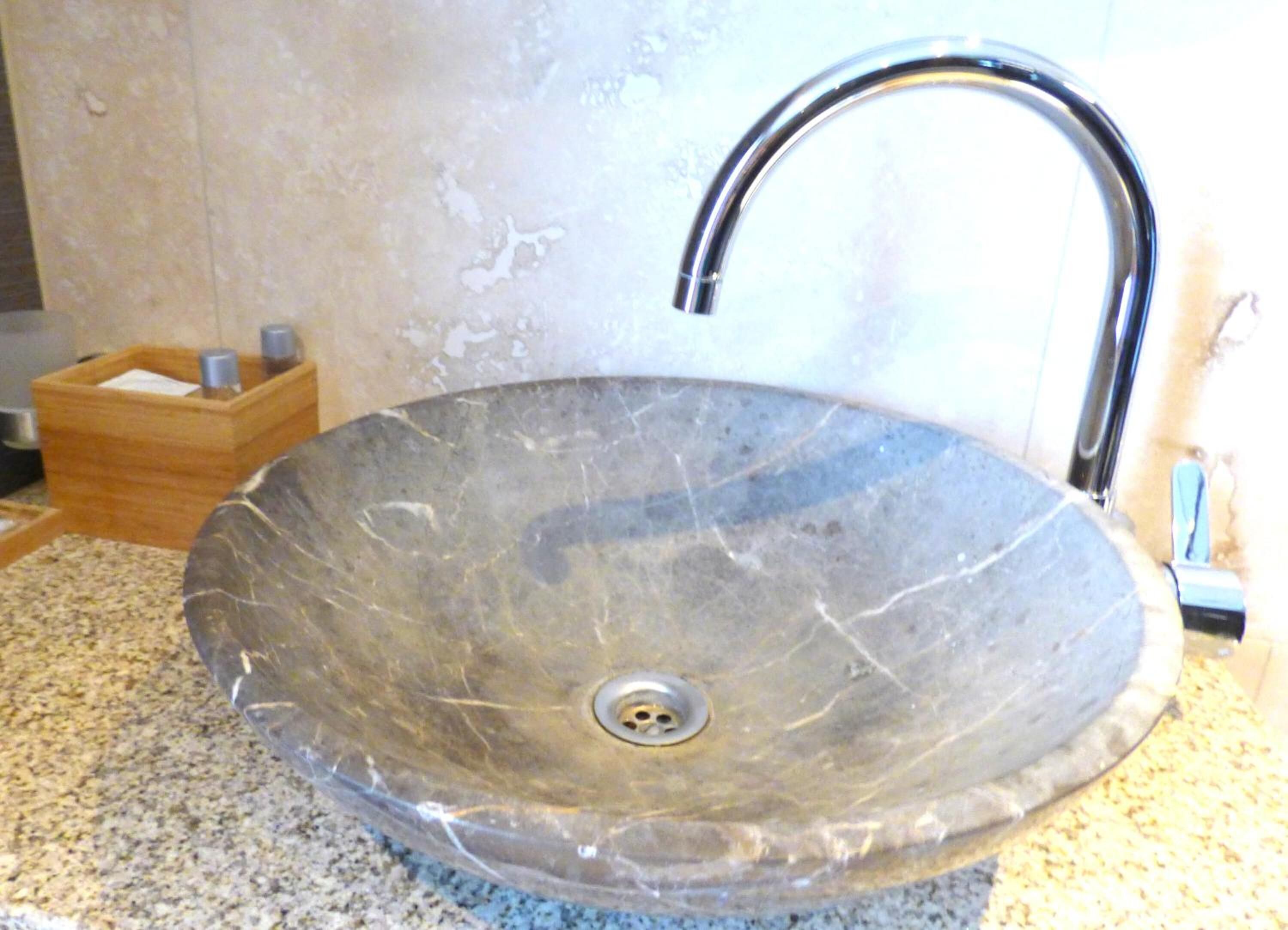 A large, oval-shaped, clear glass sink with a single faucet on a granite countertop.