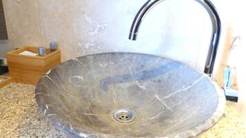 A large, oval-shaped, clear glass sink with a single faucet on a granite countertop.