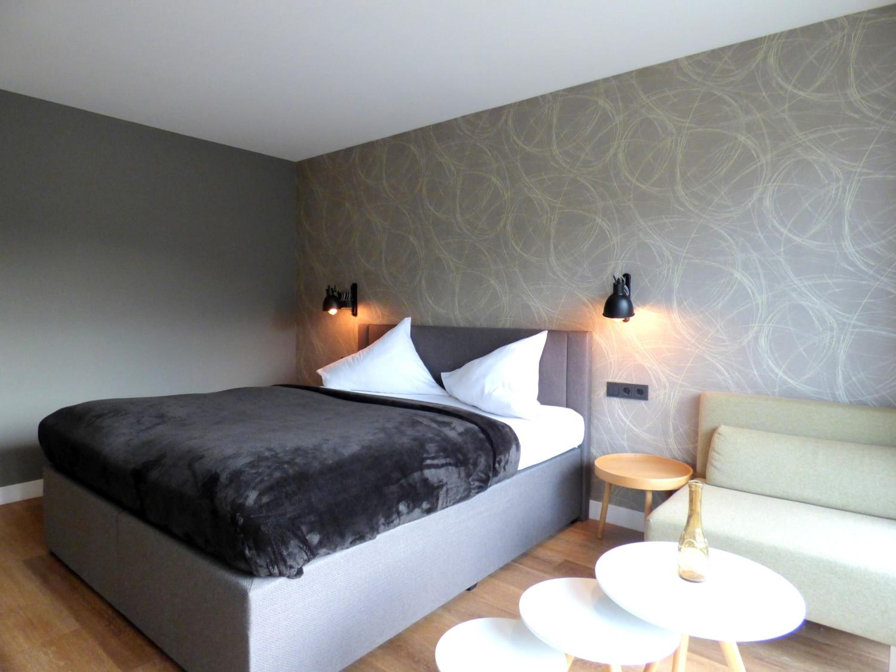 Een moderne slaapkamer met een groot bed, twee bedlampen, een klein rond tafeltje en een bank.