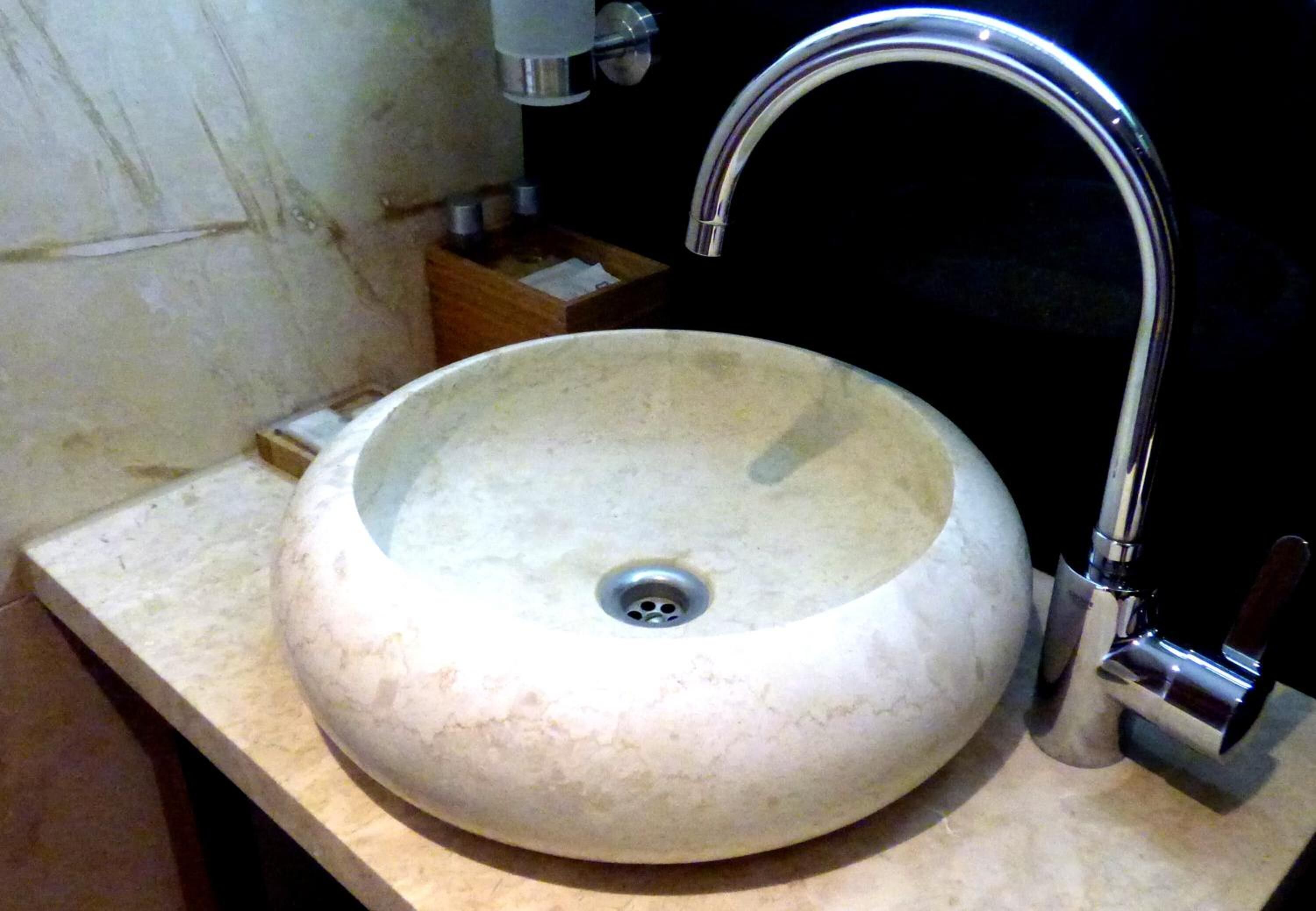 A round, white ceramic sink with a single faucet on a beige countertop.