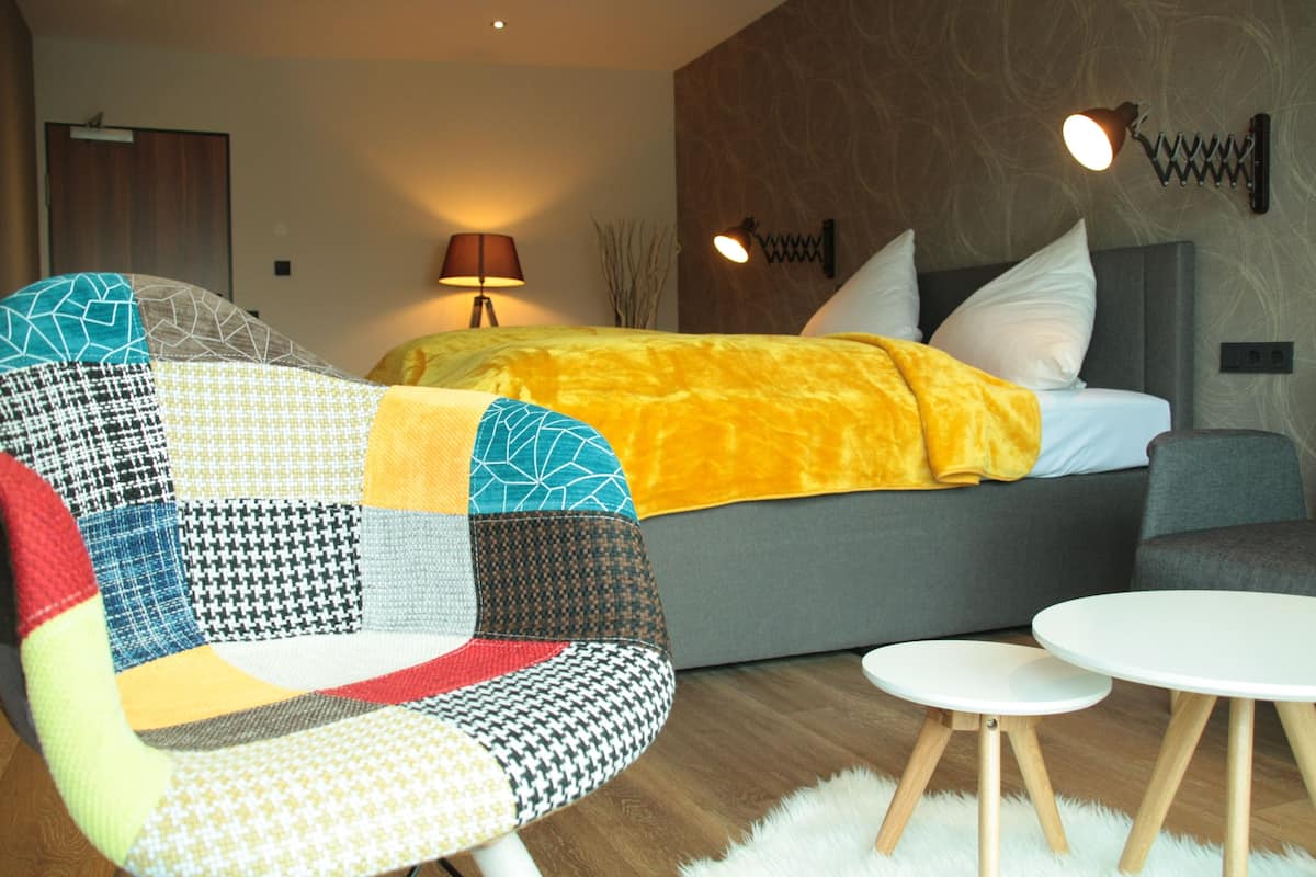 A modern bedroom with a bed, a colorful chair, a small white table, and a lamp.
