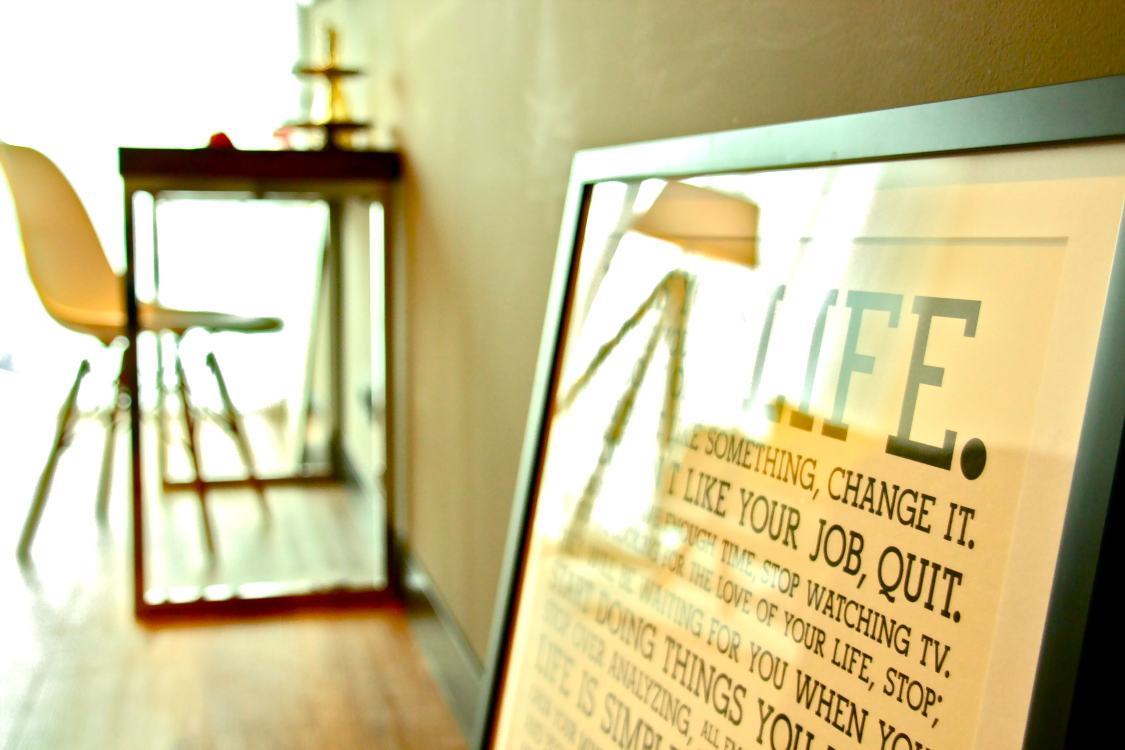 A framed inspirational quote on a wall in a room with a chair and a table.