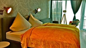 A modern bedroom with a neatly made bed, a bedside lamp, and a view of the outdoors through sheer curtains.