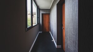Un pasillo con un ventanal grande, una puerta de madera y un muro con textura.
