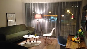 Una sala moderna con un sofá verde, una silla blanca, una mesita redonda y una mesa de comedor con fruta.