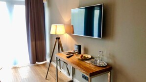 Habitación de hotel con escritorio de madera, televisor de pantalla plana, lámpara y ventana con cortinas.
