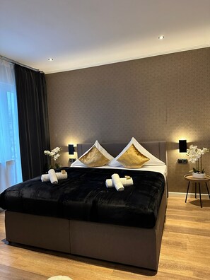 A modern bedroom with a large bed, dark curtains, and a small side table with a plant. - Niteroom Boutiquehotel (Duisburg)