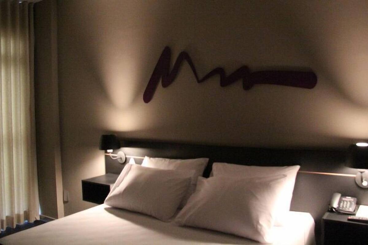 A hotel room with a large bed, two pillows, a nightstand with a phone, and a wall with a decorative sign.