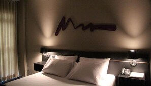 A hotel room with a large bed, two pillows, a nightstand with a phone, and a wall with a decorative sign. - Vista Inn Express Contagem (Contagem)
