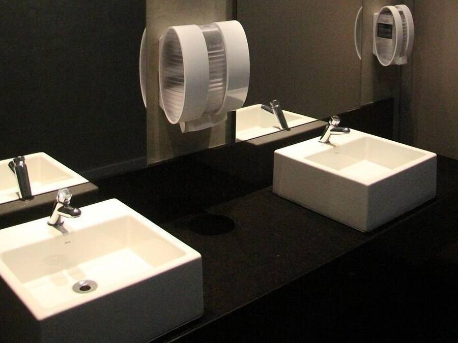 Deux éviers blancs dotés de robinets modernes, un plan de travail foncé et un miroir qui reflète les éviers.